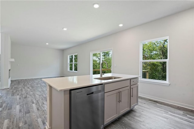 kitchen with stainless steel dishwasher, a sink, gray cabinets, light wood-style floors, and light countertops