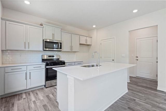 kitchen featuring stainless steel appliances, a sink, light wood-type flooring, an island with sink, and light countertops