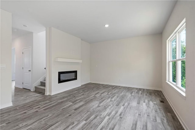 unfurnished living room featuring wood finished floors, plenty of natural light, stairs, a glass covered fireplace, and recessed lighting