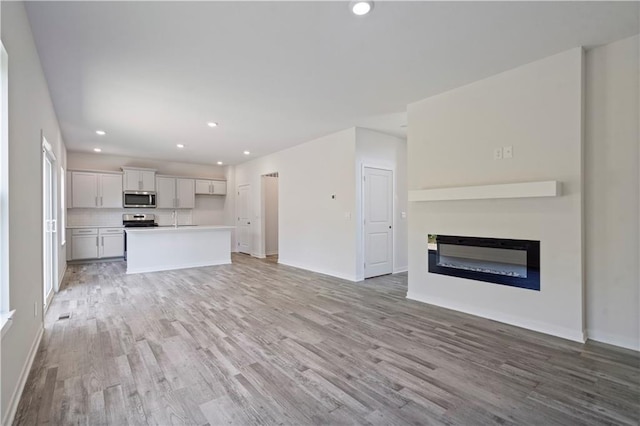 unfurnished living room with light wood finished floors, recessed lighting, baseboards, a glass covered fireplace, and a sink