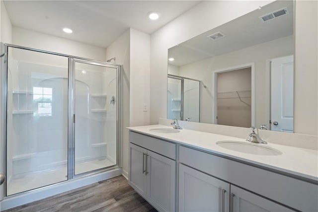 full bathroom featuring a stall shower, wood finished floors, double vanity, a spacious closet, and recessed lighting