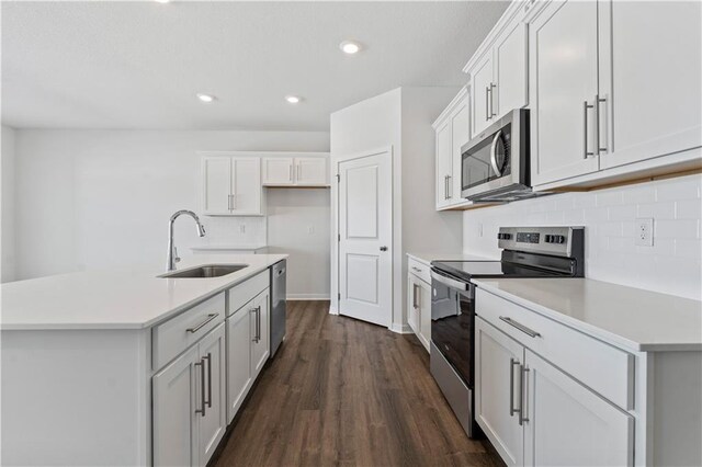 kitchen featuring stainless steel appliances, a sink, backsplash, dark wood-style floors, and light countertops