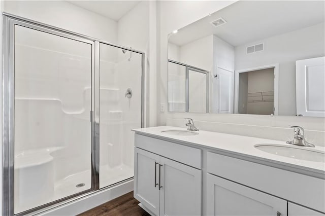 full bathroom with a stall shower, double vanity, wood finished floors, and a walk in closet