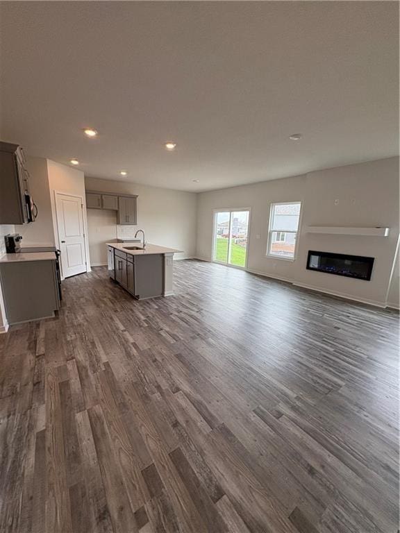 unfurnished living room with dark wood-type flooring, a sink, recessed lighting, a glass covered fireplace, and baseboards