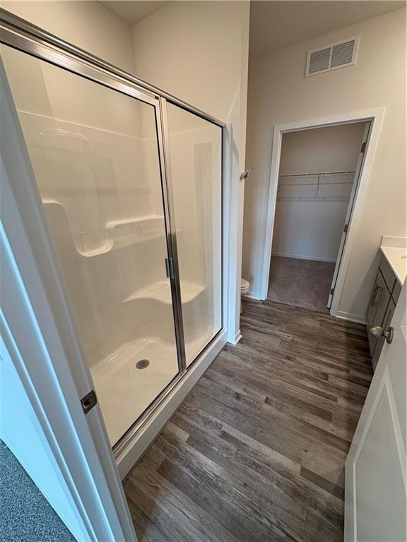 full bath featuring a stall shower, wood finished floors, toilet, and a walk in closet