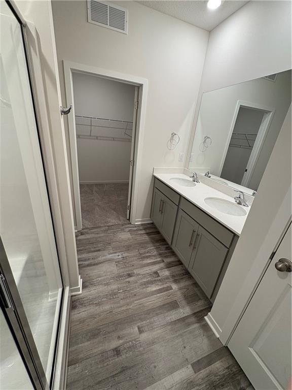 bathroom featuring wood finished floors, double vanity, a spacious closet, and recessed lighting