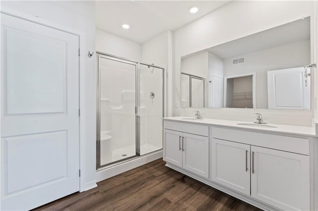 bathroom featuring a shower stall, double vanity, wood finished floors, and recessed lighting