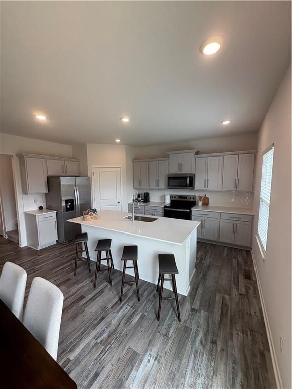 kitchen featuring appliances with stainless steel finishes, a sink, a kitchen bar, dark wood-style flooring, and recessed lighting