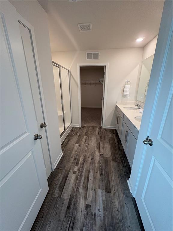 bathroom featuring a stall shower, wood finished floors, vanity, and a walk in closet
