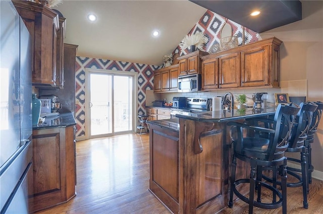 10111 N Tullis Dr, Kansas City, MO 64157 - kitchen featuring appliances with stainless steel finishes, vaulted ceiling, brown cabinetry, light wood-style flooring, and a breakfast bar area