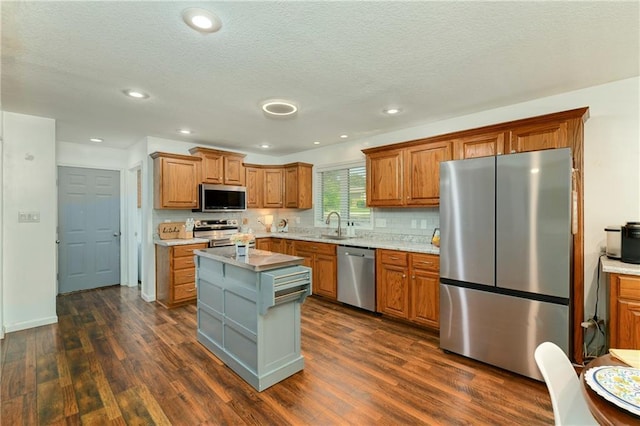 kitchen with appliances with stainless steel finishes, a sink, dark wood-style floors, brown cabinetry, and a kitchen island