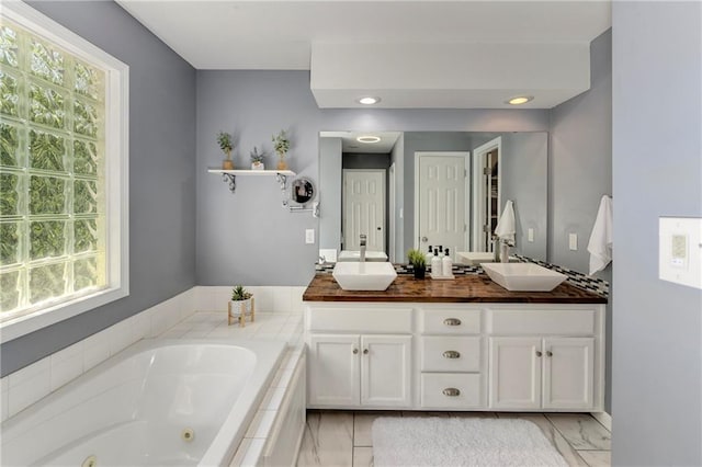 bathroom featuring marble finish floors, a whirlpool tub, double vanity, and recessed lighting