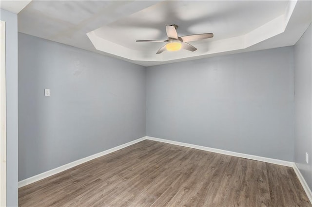 spare room with a tray ceiling, wood finished floors, a ceiling fan, baseboards, and a skylight