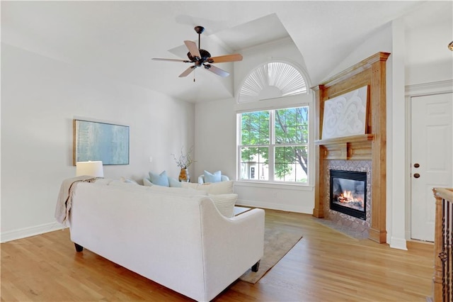 living room with vaulted ceiling, a high end fireplace, a ceiling fan, light wood-style floors, and baseboards