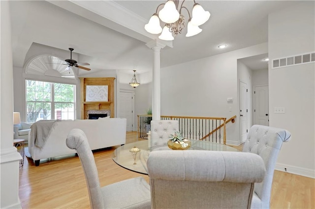 dining area featuring a ceiling fan, a chandelier, light wood-style floors, baseboards, and a fireplace