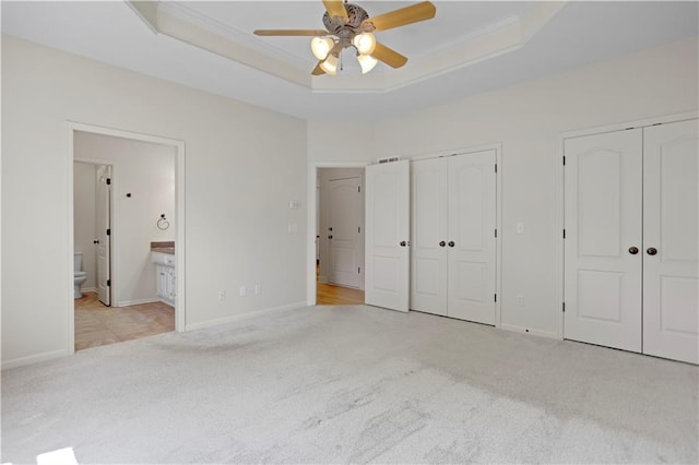 unfurnished bedroom featuring two closets, carpet, connected bathroom, a raised ceiling, and crown molding
