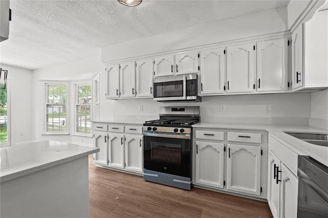 13300 Palmer Ave, Grandview, MO 64030 - kitchen featuring appliances with stainless steel finishes, a textured ceiling, white cabinets, dark wood-type flooring, and light countertops