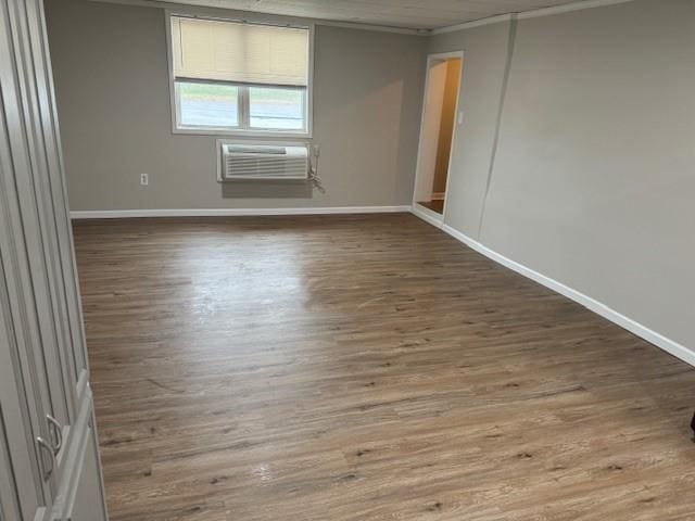 unfurnished room featuring ornamental molding, baseboards, wood finished floors, and an AC wall unit