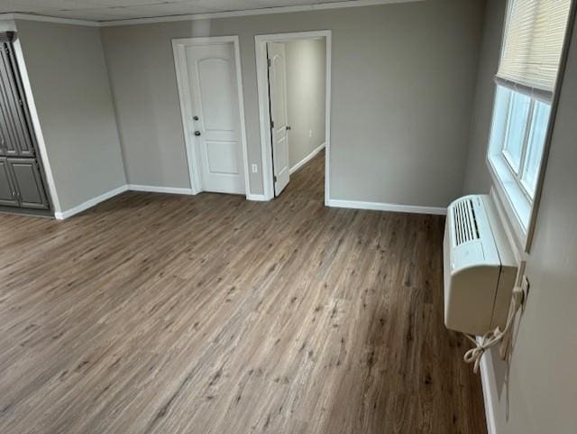 unfurnished room with ornamental molding, baseboards, wood finished floors, and a wall mounted air conditioner