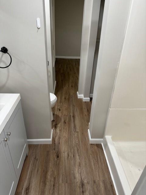 bathroom with wood finished floors, vanity, toilet, baseboards, and a shower