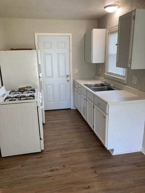 kitchen with a sink, white gas stove, dark wood-style floors, light countertops, and white cabinetry
