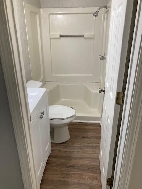 bathroom with a shower, wood finished floors, toilet, and vanity
