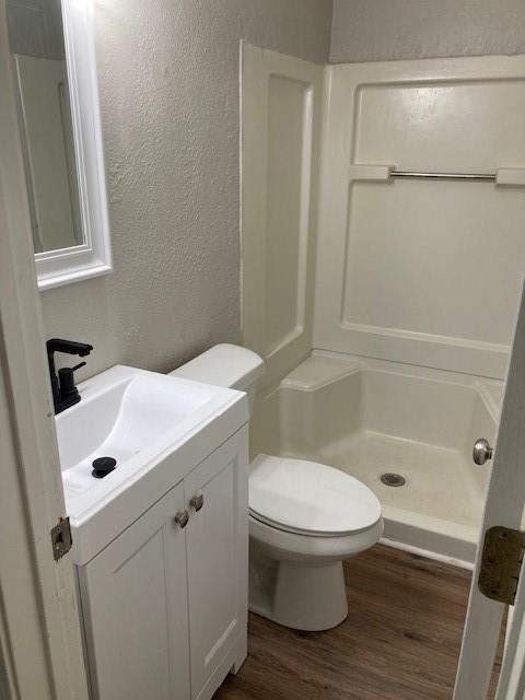 bathroom with a textured wall, wood finished floors, a stall shower, vanity, and toilet