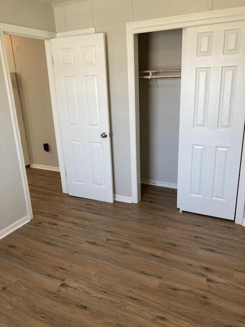unfurnished bedroom featuring baseboards, dark wood-style floors, and a closet