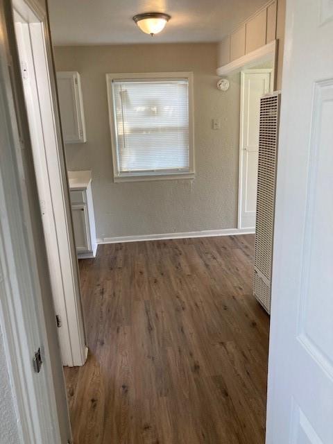 hallway featuring a heating unit, wood finished floors, and baseboards