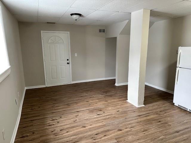 basement featuring freestanding refrigerator, wood finished floors, baseboards, and a drop ceiling