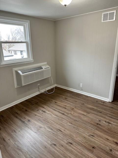 unfurnished room with baseboards, wood finished floors, ornamental molding, and an AC wall unit