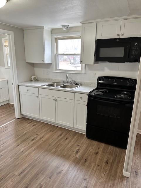kitchen with black appliances, a sink, light wood finished floors, and white cabinets