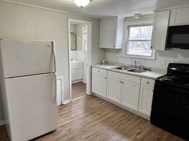 kitchen with black appliances, a sink, light countertops, light wood-style flooring, and white cabinetry