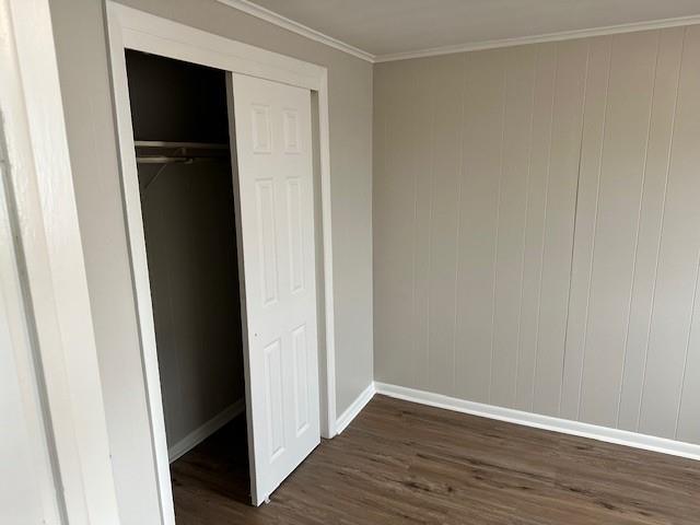 unfurnished bedroom with dark wood-style floors, baseboards, a closet, and crown molding
