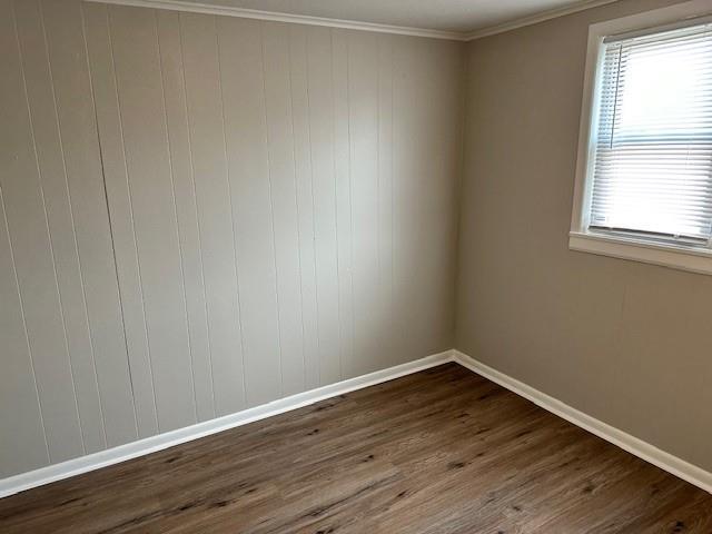 unfurnished room featuring baseboards, dark wood-type flooring, ornamental molding, and healthy amount of natural light