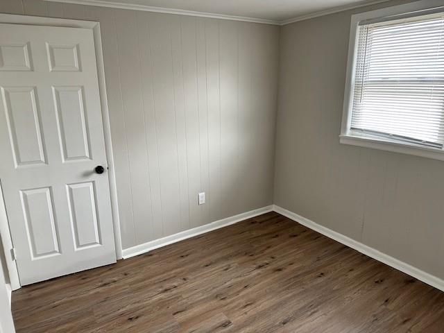 empty room featuring baseboards, dark wood-type flooring, and crown molding