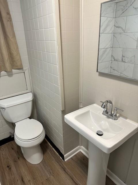 bathroom featuring wood finished floors, toilet, and tile walls