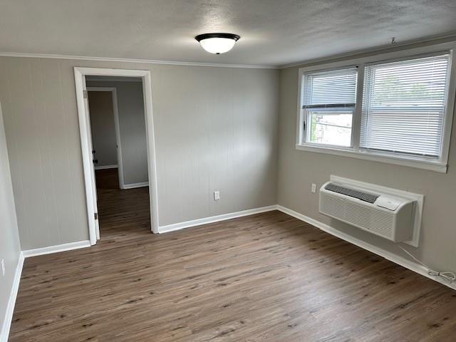 unfurnished room featuring a wall mounted air conditioner, baseboards, wood finished floors, and ornamental molding