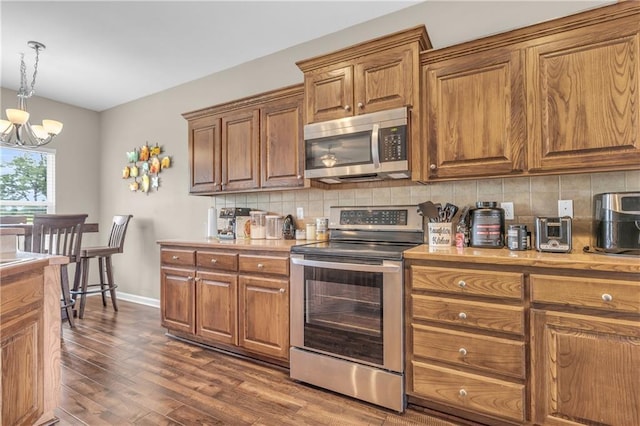 21923 W 116th Pl, Olathe, KS 66061 - kitchen featuring appliances with stainless steel finishes, brown cabinets, a chandelier, and tasteful backsplash