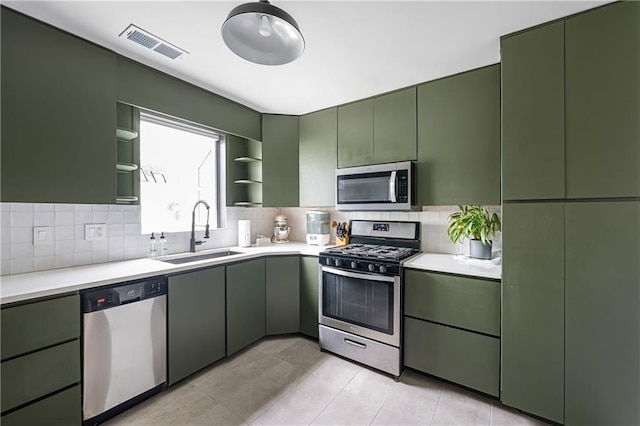 831 E 25th Ave, North Kansas City, MO 64116 - kitchen featuring appliances with stainless steel finishes, green cabinetry, open shelves, a sink, and light countertops