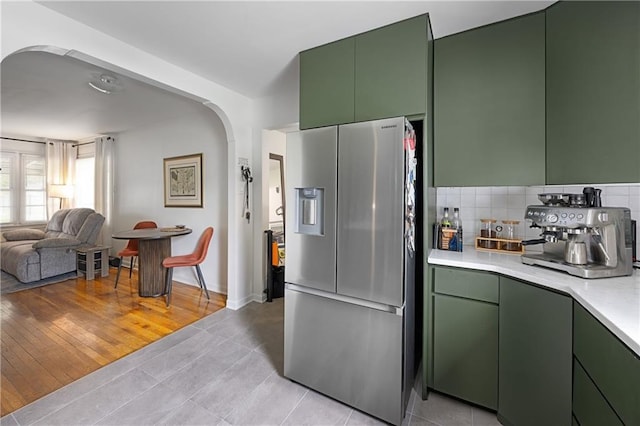 831 E 25th Ave, North Kansas City, MO 64116 - kitchen with stainless steel fridge with ice dispenser, green cabinetry, arched walkways, light countertops, and open floor plan