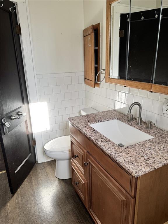 bathroom featuring tile walls, toilet, wood finished floors, a wainscoted wall, and vanity
