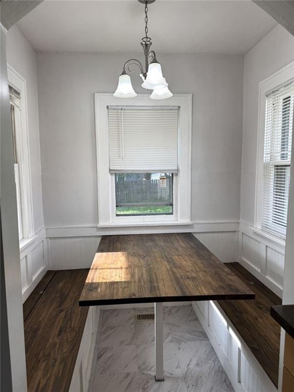 unfurnished dining area featuring a chandelier, a wainscoted wall, dark marble finish flooring, and a decorative wall