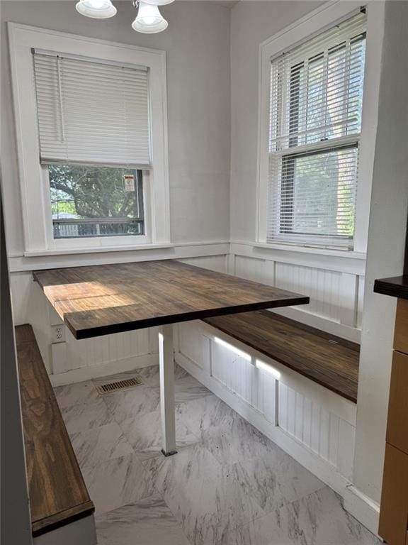 unfurnished dining area with marble finish floors, a decorative wall, and wainscoting