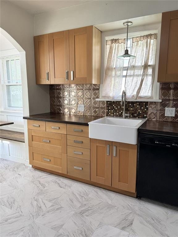 kitchen with dishwasher, a sink, arched walkways, decorative backsplash, and dark countertops