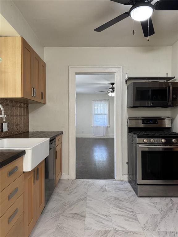 kitchen with stainless steel appliances, ceiling fan, dark countertops, a sink, and backsplash