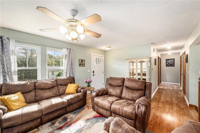 living room with wood finished floors, ceiling fan, a textured ceiling, and baseboards