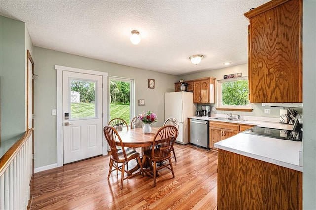 kitchen with stainless steel dishwasher, freestanding refrigerator, a sink, light wood-type flooring, and a textured ceiling
