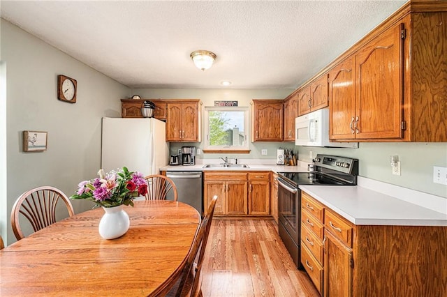 kitchen featuring stainless steel appliances, a sink, light wood-style floors, brown cabinetry, and light countertops