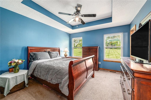 bedroom with a textured ceiling, light carpet, a raised ceiling, baseboards, and a ceiling fan